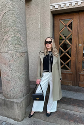 a lady in a black knit top, a pair of white wide leg pants and a grey unisex coat